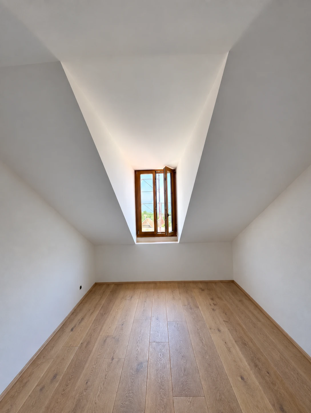 Pièce sous combles avec lucarne, murs blancs et parquet en bois